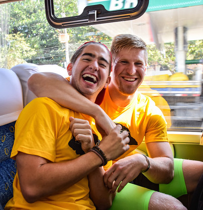 Juan Carlos Serrano sits with a fellow VOLeader on a bus. Both are laughing while looking at the camera and hugging.e