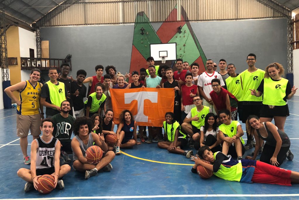 Ashleigh Huffman, former CSPS asst. director, poses holding a Tennessee flag with basketball players in Brazil