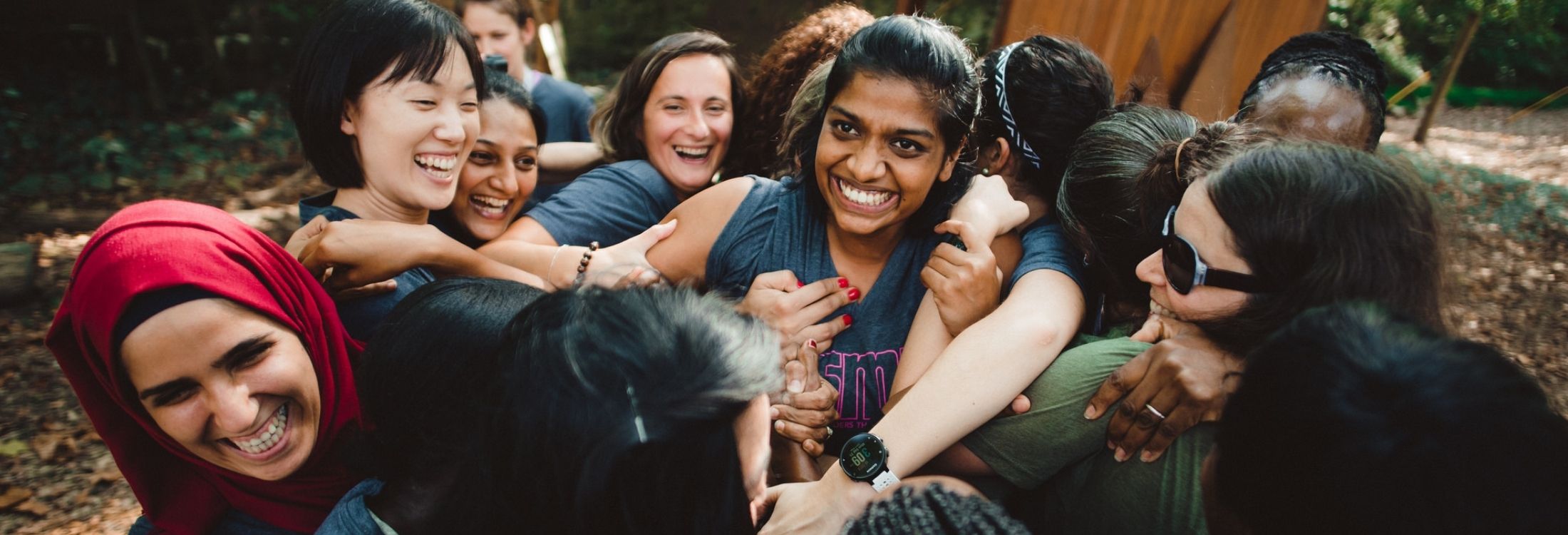 Sangeetha Manoharan from India, a participant in the 2017 Global Sports Mentoring Empowering Women program, stands grinning in the middle of a huddle of all program participants as they navigate a ropes course challenge at Terrapin Adventures.